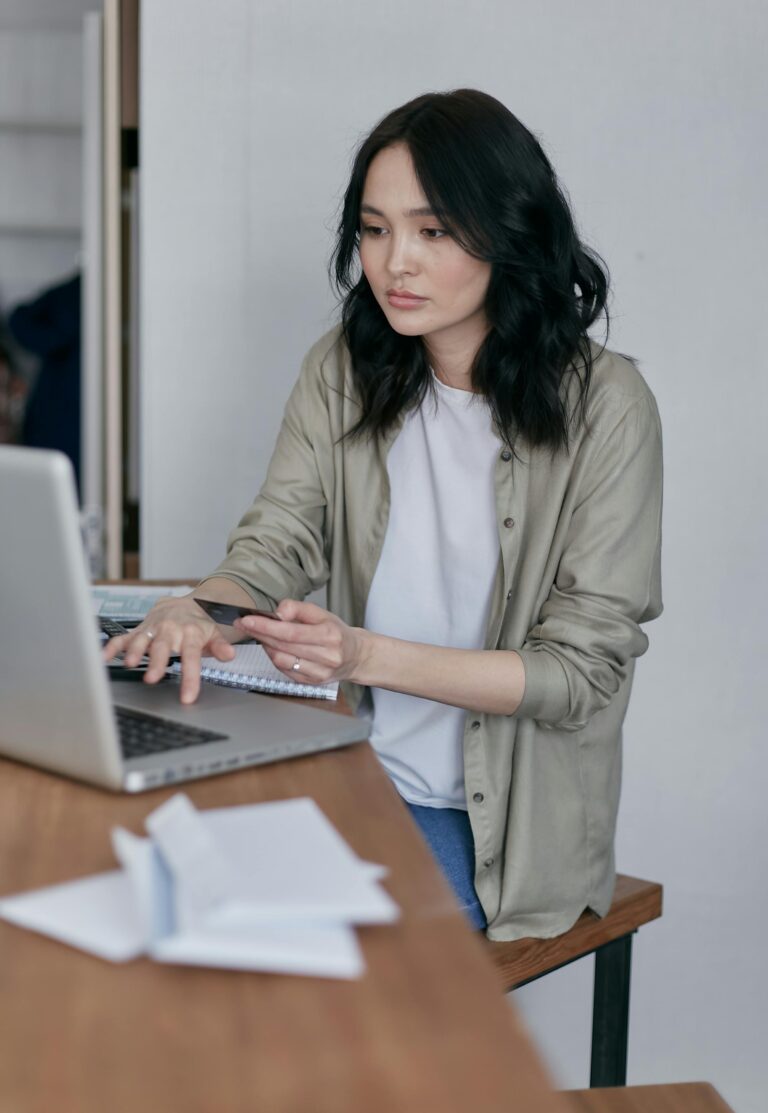 Asian woman working on laptop with bills on table, managing finances.